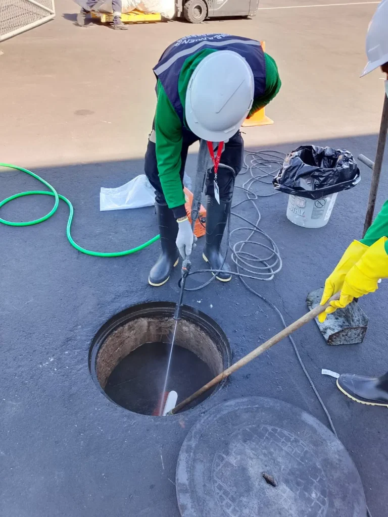 Técnicos lavando el interior de un pozo séptico con hidrolavadora y cepillo