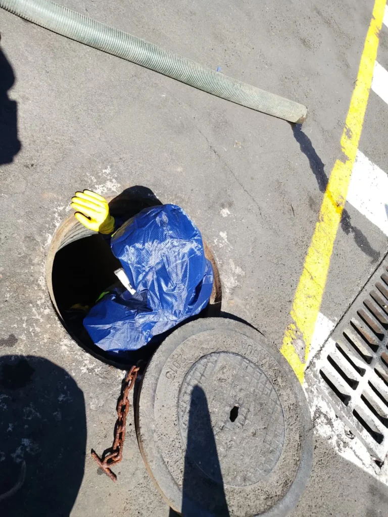 Técnico con traje de protección y guantes ingresando a un pozo séptico para su limpieza