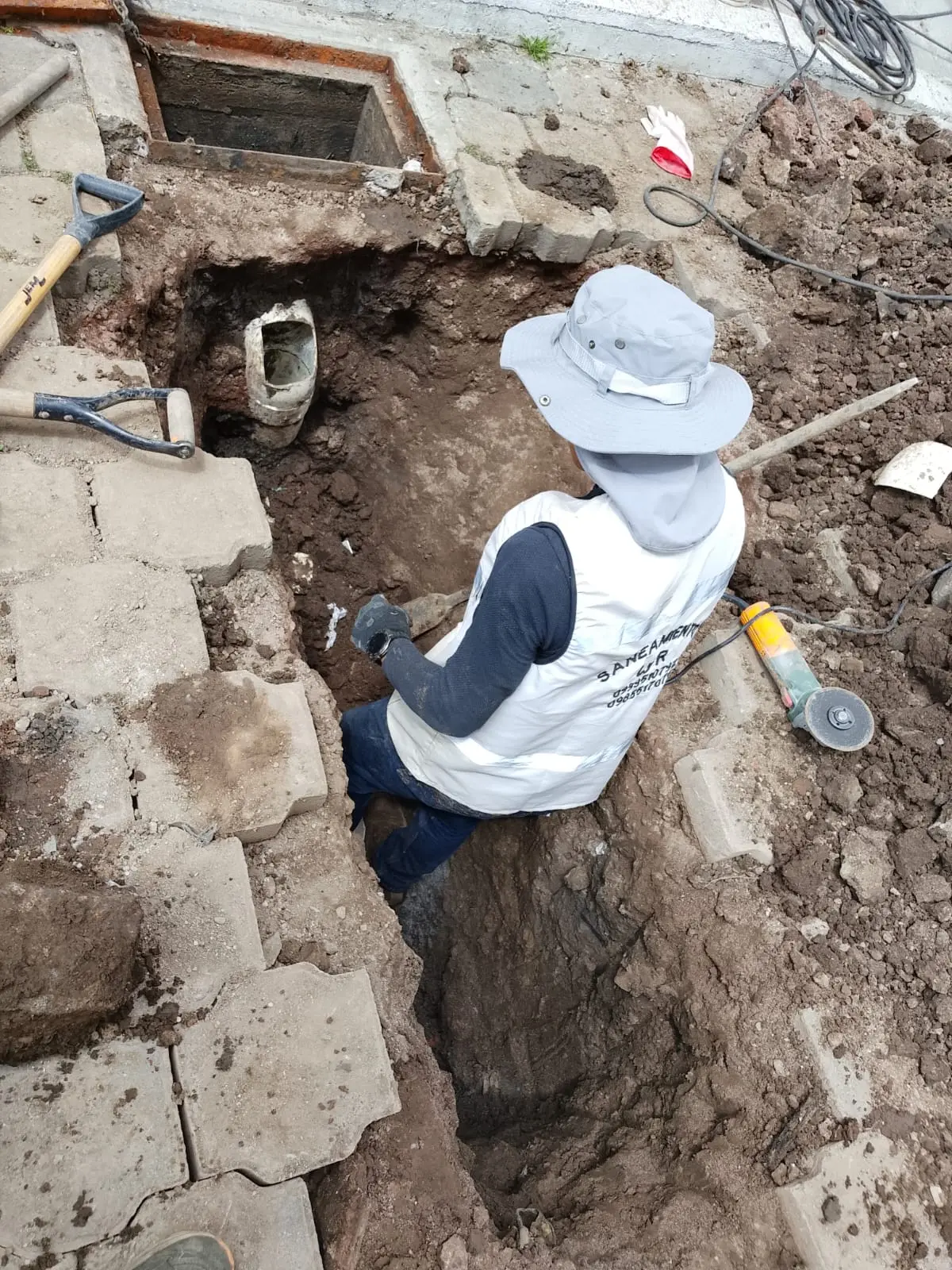 Técnico excavando hasta la tubería de un pozo séptico con pala y herramientas