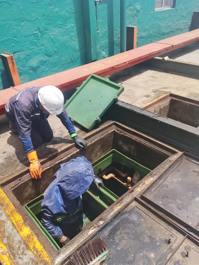 Técnico dentro de una trampa de grasa industrial durante el mantenimiento de tuberías